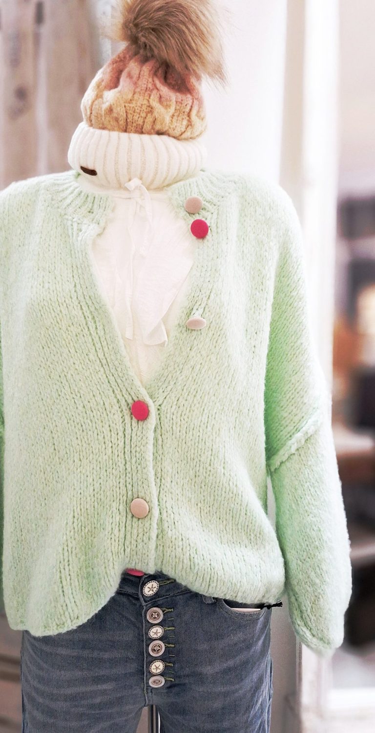 Mintfarbener, lockerer Cardigan mit rosa Knöpfen über einer weißen Rüschenbluse.