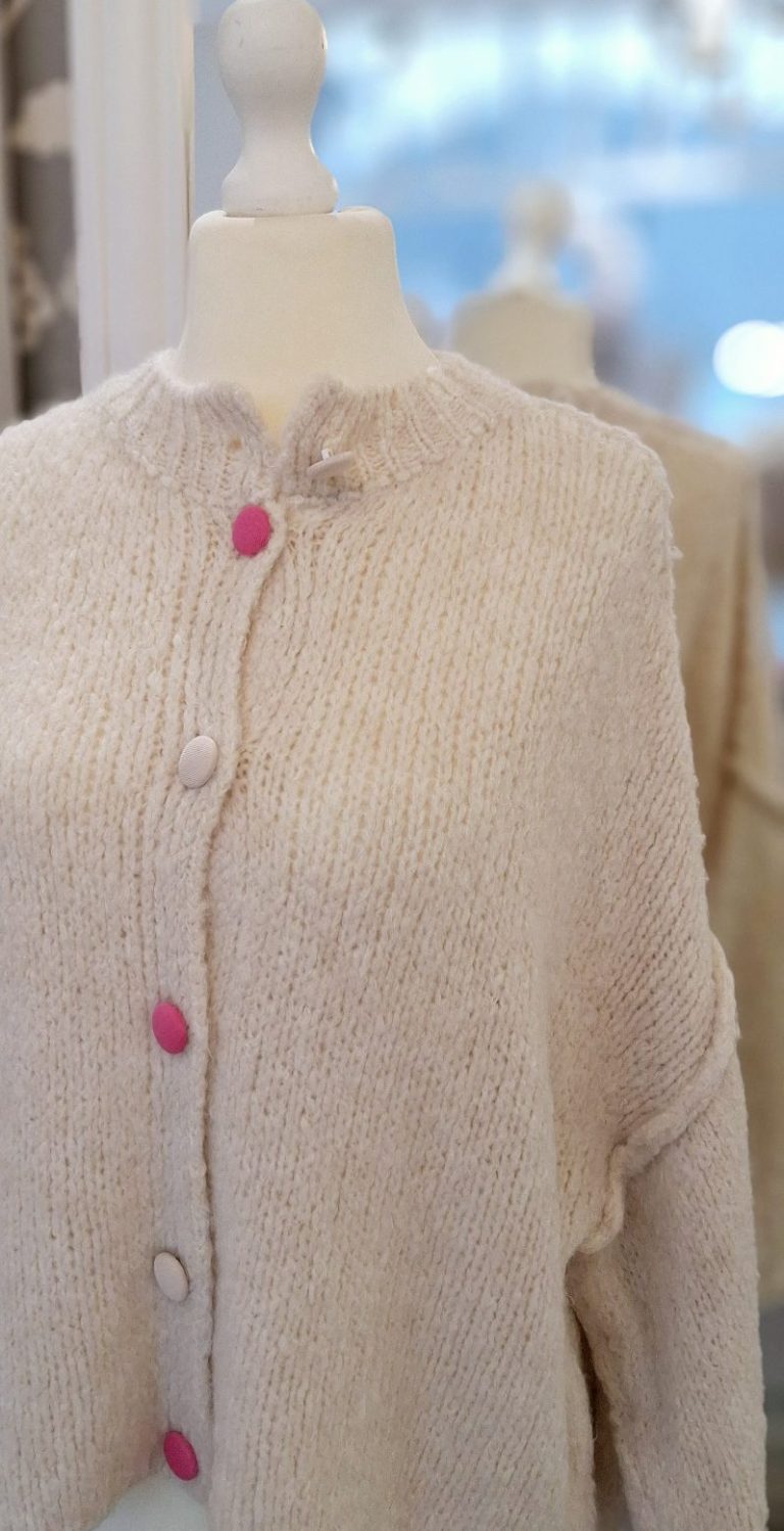 Beige Strickjacke mit verschiedenen pinken und sandfarbenden Knöpfen, auf einer Schneiderpuppe.